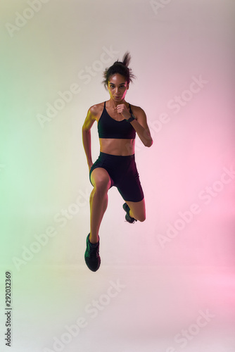 Do it Full length of young athlete woman with perfect body in sports clothing jumping in studio against colorful background