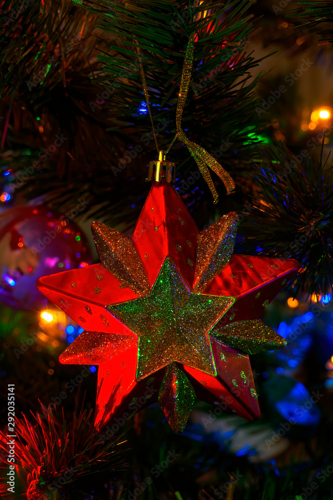 Red toy in the form of a star hangs on a christmas tree with garlands