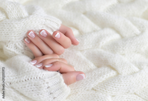 Women's beautiful hands with French manicure on the background of a white warm sweater