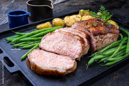 Traditional roasted dry aged veal tenderloin with beans and potatoes offered as closeup on a modern design cast iron tray photo