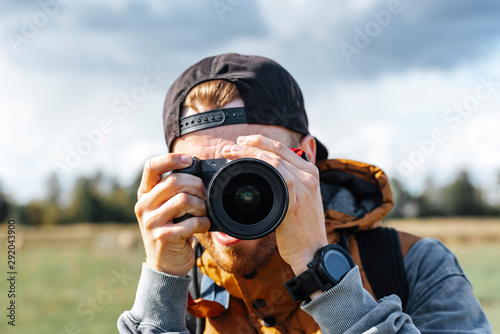 Photographer in brown vest and black hat taking pictures with his camera during sunny summer day.  © valdisskudre
