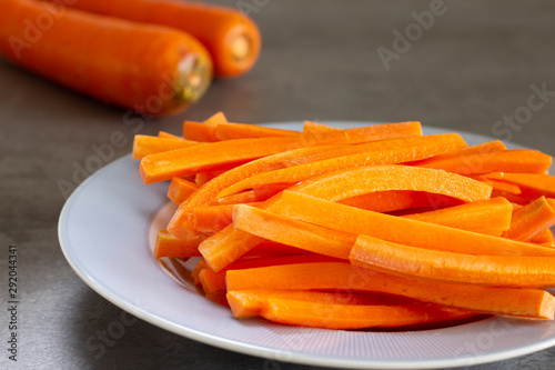 carrot sticks in blue rim dish with carrots in the background on gray surface