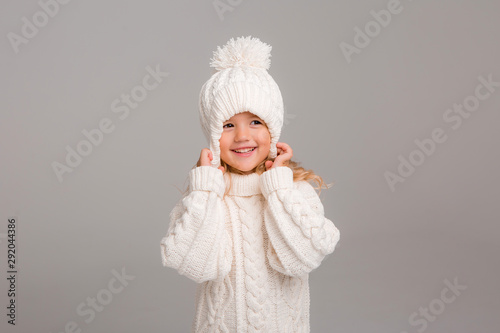 Winter clothes. Portrait of a little curly-haired girl in a knitted white winter hat. little blonde girl in white knitted hat and sweater smiling light background isolate, space for text