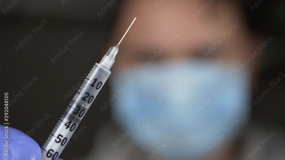 Doctor in medical mask on face and blue gloves offers syringe with vaccine or medicine Doctor in medical mask on face and blue gloves offers syringe with vaccine or medicine