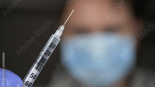 Doctor in medical mask on face and blue gloves offers syringe with vaccine or medicine photo