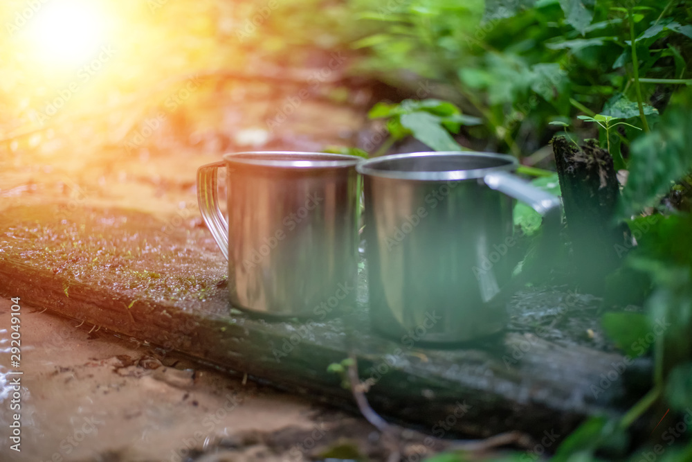 Two metal mugs stand on a shelf across a stream in the forest close-up. Photo with illumination, light