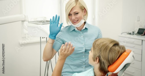Friendly smiling female dentist giving teenage boy high-five after successful procedure, oral cavity checkup