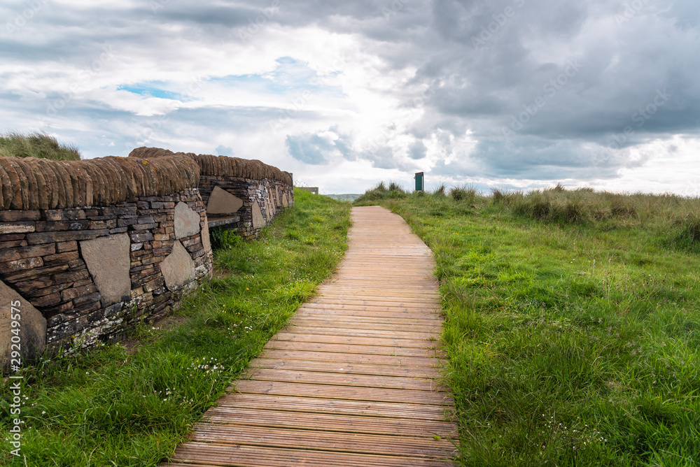 Fototapeta premium Empty boardwalk lined with a stone wall in a seaside park on a cloudy spring day