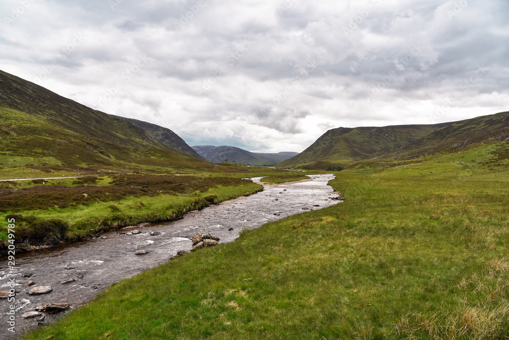 River in the Scottish Highlands on an overcast summer day. A road runs alongside the river.