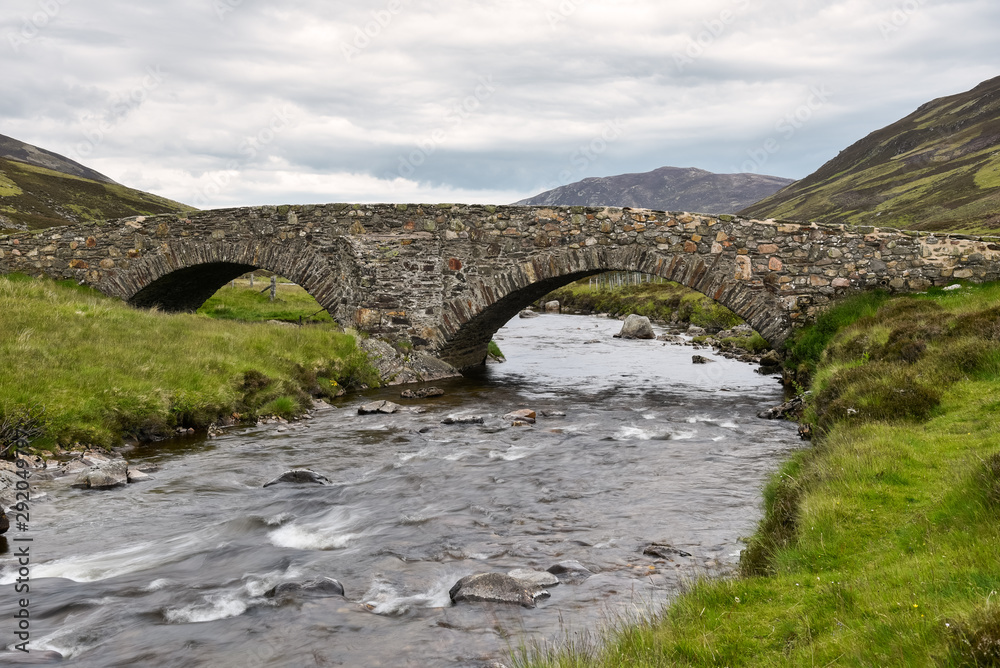 Old stone bridge over a stream in the Scottish Highlands on a cloudy summer day