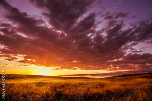 Amazing yellow, purple, piink and orange sunset over an empty field of dry grass surrounded by hills in a rural area.