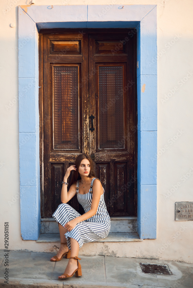 Fototapeta premium Young stylish woman sitting against old wooden doorway on the street.