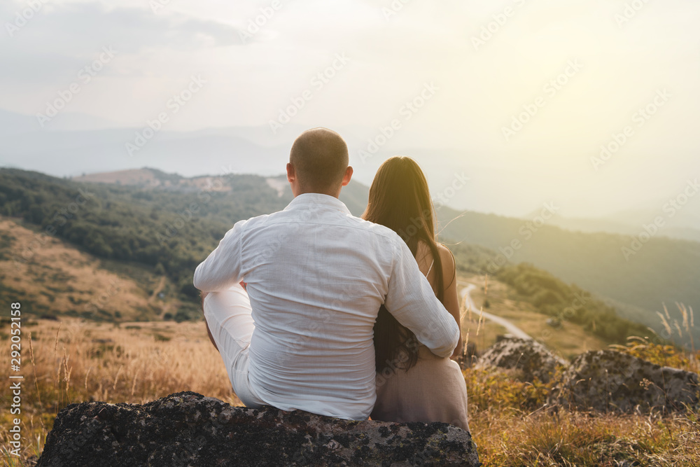 Back viw of young couple man and woman girl hugging embracing in nature on mountain range in autumn day evening field
