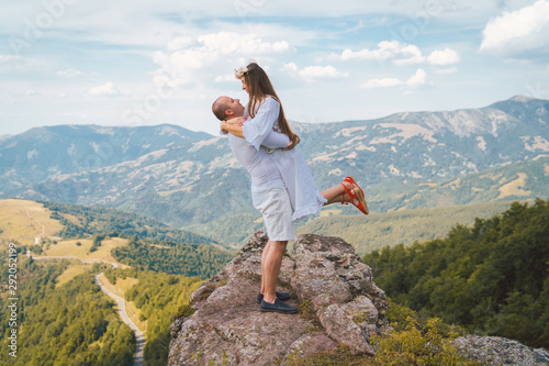 Young couple wearing white on the top of the mountain rock man holding his girl friend wife fiancee up hugging and kissing couple in love