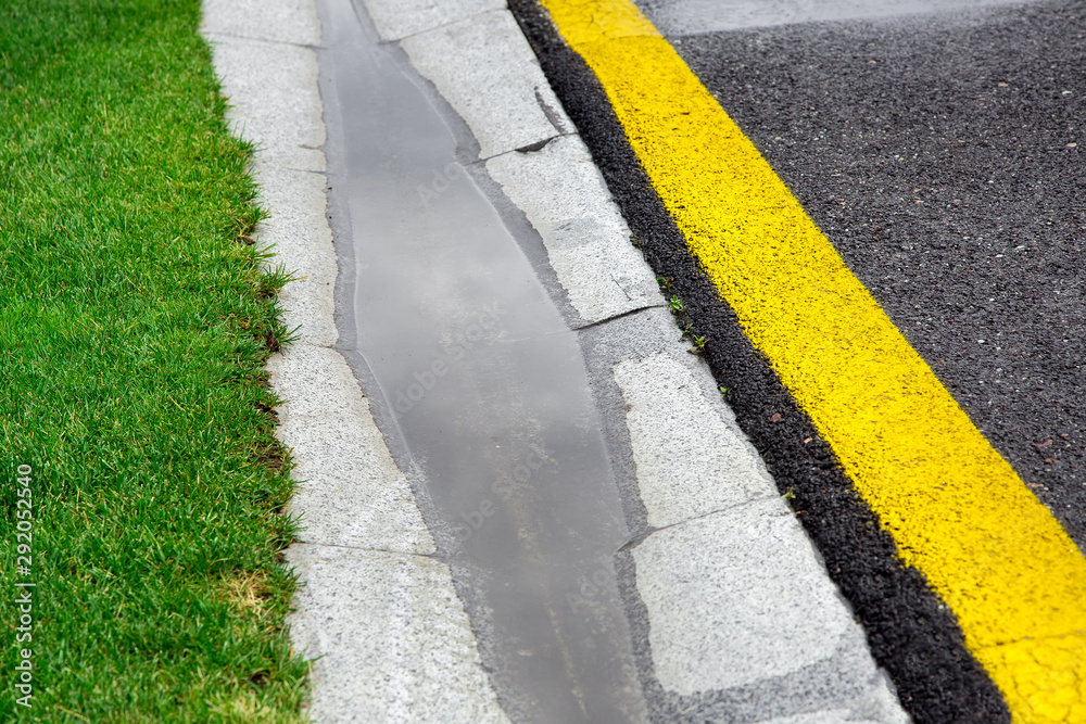 Obraz premium the current rainwater in the filled canal is a cement ditch of the drainage system on the side of a wet asphalt road after rain.