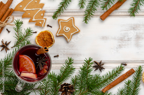 Hot red mulled wine or gluhwein in glass with orange, cinnamon sticks and anise on white wooden background.