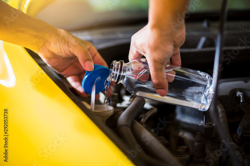 Mechanic fill fresh water into windscreen or in water tank wiper on yellow car engine room. Service and maintenance of yellow cars or vehicles.