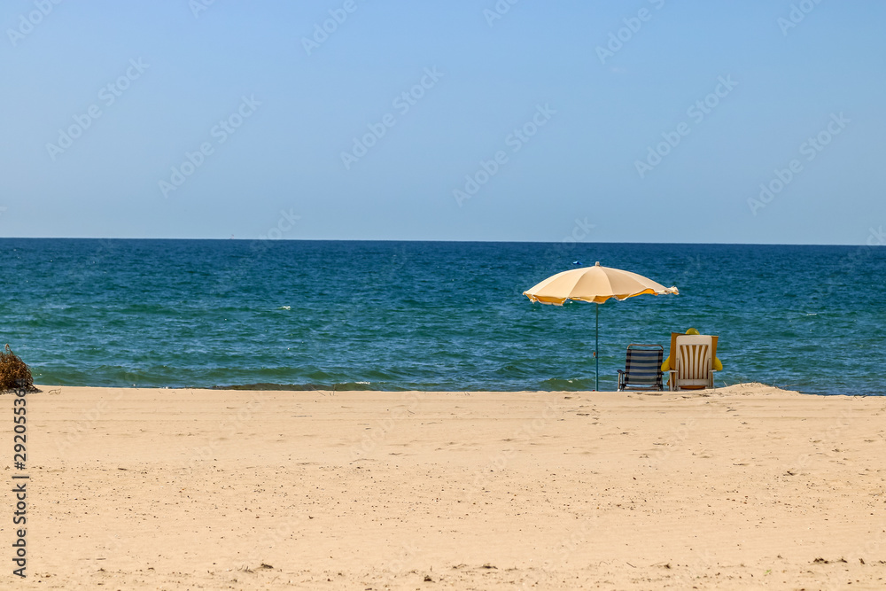 Beach umbrella and beach chair, yellow on the beach in front of the sea. Summer activity.