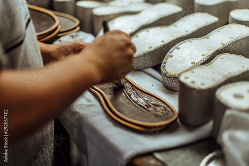 Hands of an old and experienced worker in the handmade footwear industry, performing sole gluing tasks, putting glue on the base of the shoe. photo