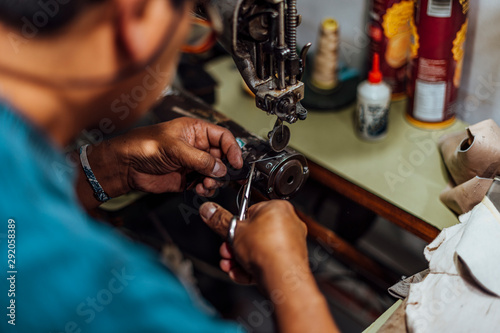 Hands of an old and experienced worker in the handmade shoe industry, performing sewing tasks on a piece of genuine leather, on a leather sewing machine.