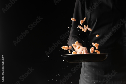 Chef cooks seafood, shrimp in a pan. On a black background for design. Freeze in motion.