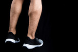 man's legs wearing training shoes on a solid black background with copy space 