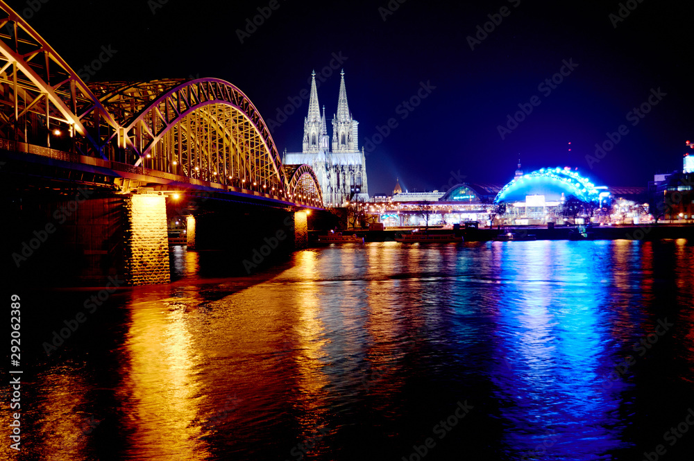 Fototapeta premium Evening view of the illuminated Cologne Cathedral and the bridge over the Rhine from the opposite bank of the river