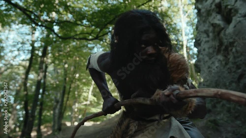 Primitive wild african man in animal fur walking slowly in the woods hunting animals for food outside cave. Prehistoric nature. Earliest human. Homo sapiens.