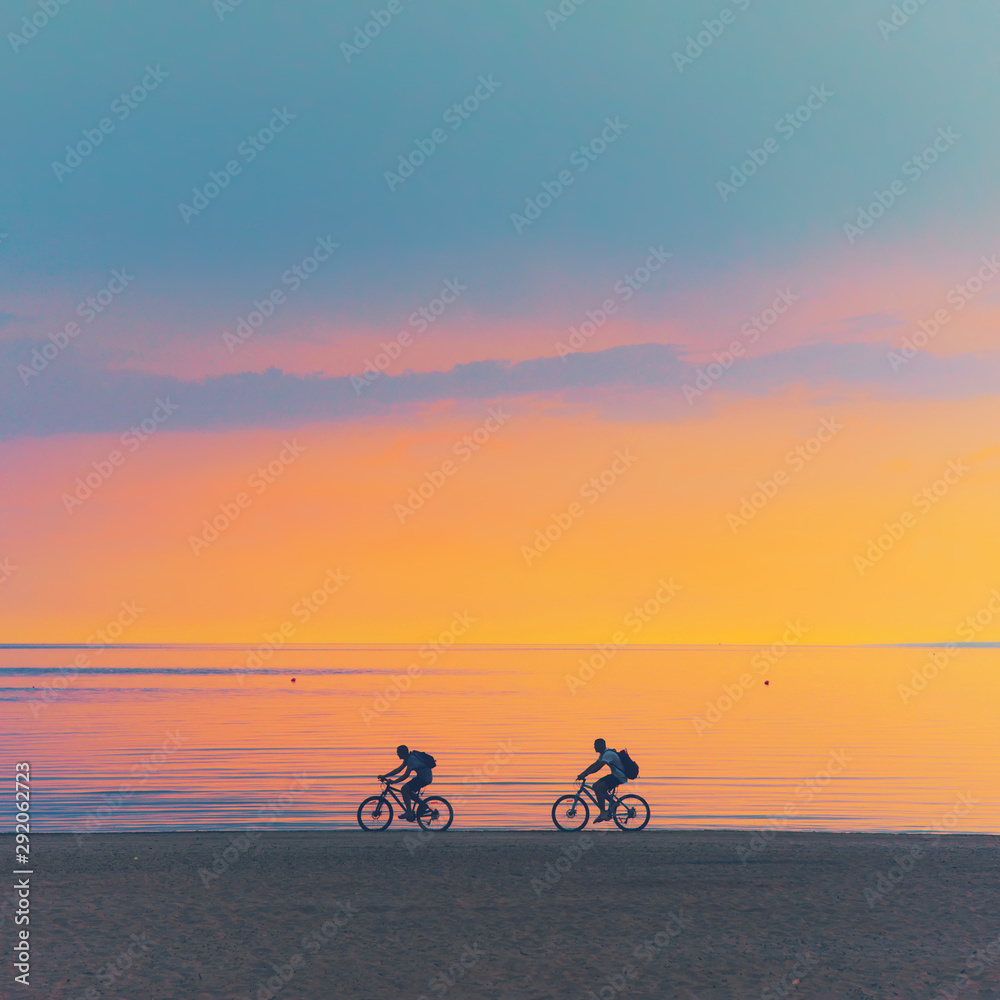 Fototapeta premium Biker silhouette riding along beach at sunset on bike Sporty company group of friends on bicycle outdoors Success achievement accomplishment and winning concept with cyclist mountain biking Copyspace