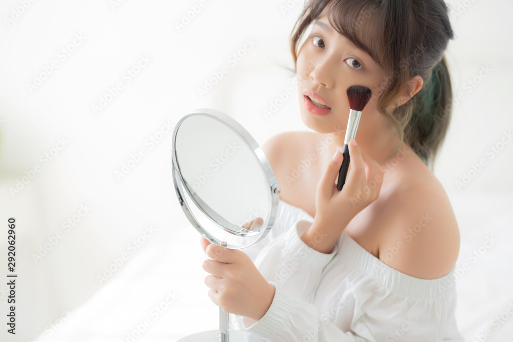Beauty portrait young asian woman smile with face looking mirror applying makeup with brush cheek in the bedroom, beautiful of girl holding blusher, skin care and cosmetic concept. Beauty portrait young asian woman smile with face looking mirror applying makeup with brush cheek in the bedroom, beautiful of girl holding blusher, skin care and cosmetic concept.