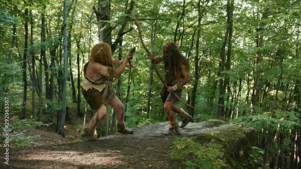 Two aggressive wildmen of neanderthals with sticks fighting for tribe leadership. Prehistoric cavemen fight in jungle forest. Rivalry concept. Wildlife of homo sapiens.