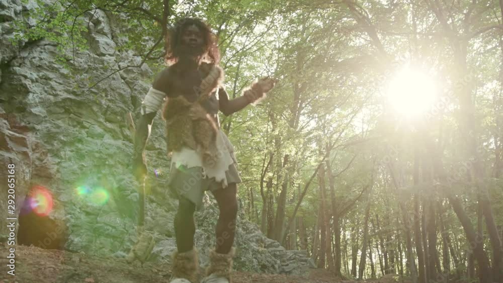 Happy african neanderthal in animal fur dancing a modern fun fance enjoying life and freedom in forest. Primitive bushman of hunter-gatherers society. Homo sapiens.