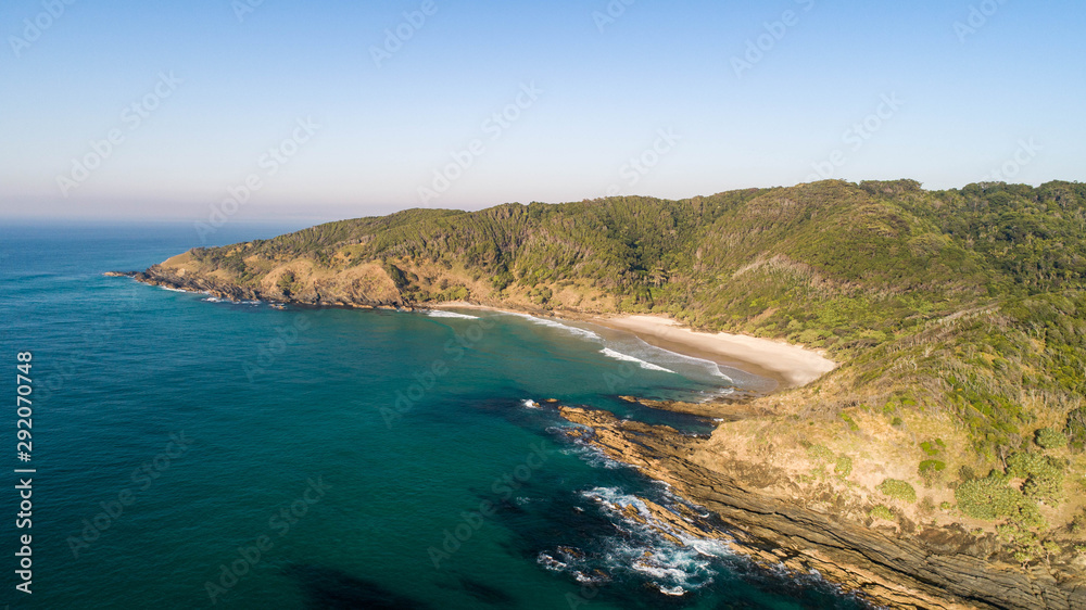 Aerial of a spectacular coastal scene with beach, ocean and cliffs on the side of a tropical forest for a beautiful holiday destination.