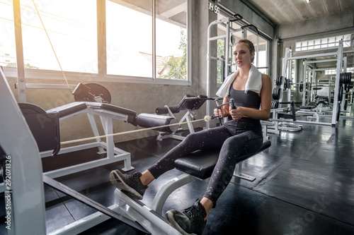 Young woman lowering weight of fitness machine and working out in the fitness gym