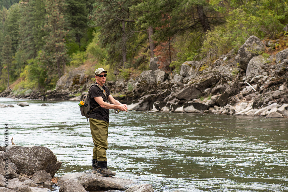 Fly fisherman casting in the mountain stream during the fall season. Fly fisherman casting in the mountain stream during the fall season.