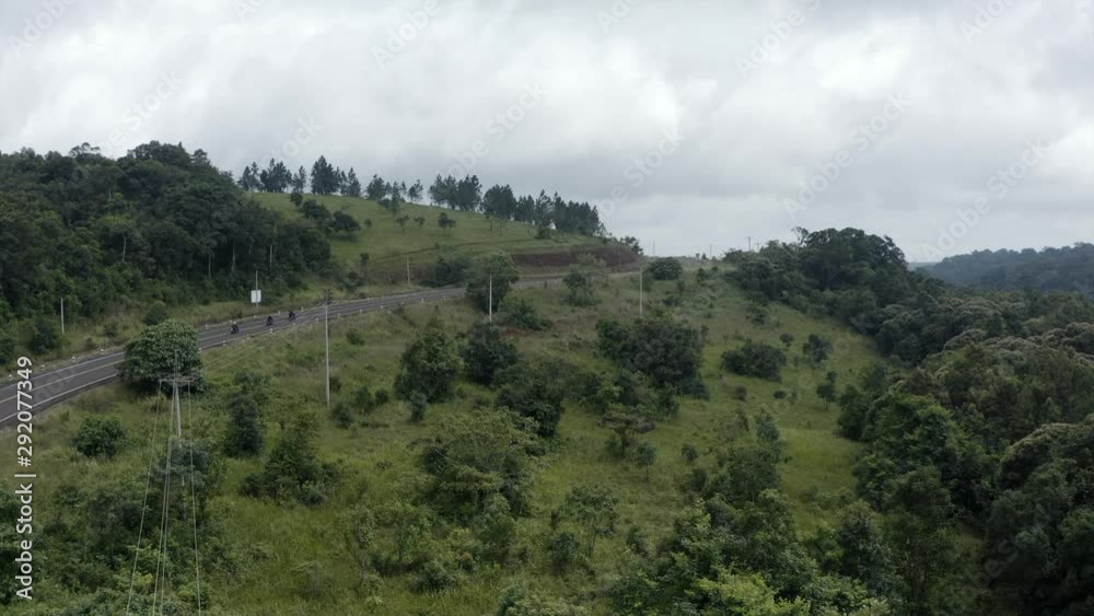 4k push in Aerial shot over a group of motorcycle rider crossing a curve hill top road surrounding by green forest 4k push in Aerial shot over a group of motorcycle rider crossing a curve hill top road surrounding by green forest