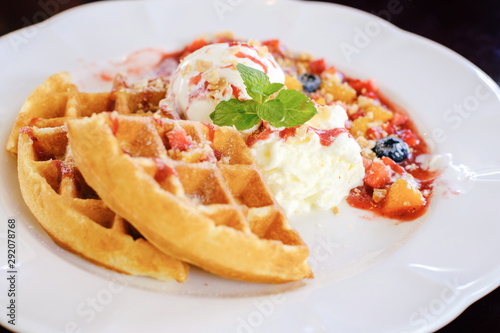 Sweet waffles with strawberries sauce vanilla ice cream fresh fruit and mint leaf on white plate at cafe restaurant in holiday summertime.