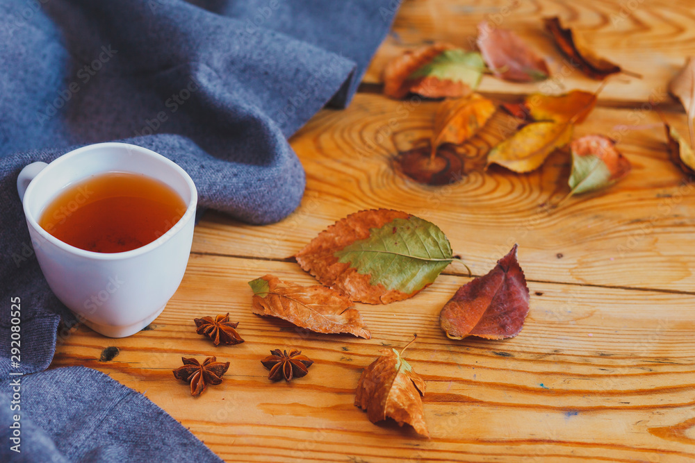 Cold autumn days. A cup of tea with fall leafs on wooden table. Warming tea on a wooden table