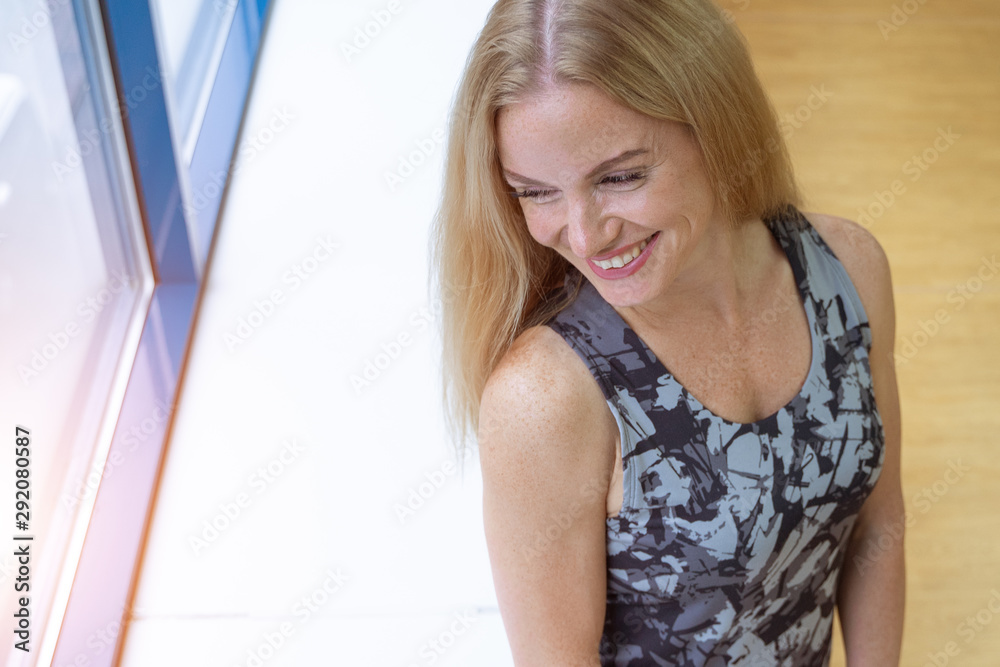 The girl with red hair in a sports uniform stands at the window and smiles radiantly