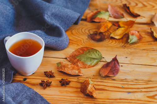 Cold autumn days. A cup of tea with fall leafs on wooden table. Warming tea on a wooden table