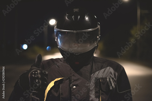 Fototapeta Naklejka Na Ścianę i Meble -  Motorbiker is showing a thumbs up over night road background.