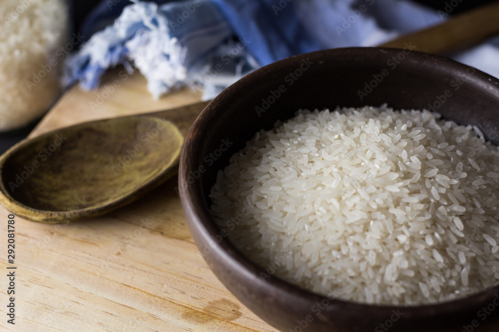 Uncooked rice in clay bowl on a wooden table with black background. Uncooked rice in clay bowl on a wooden table with black background.
