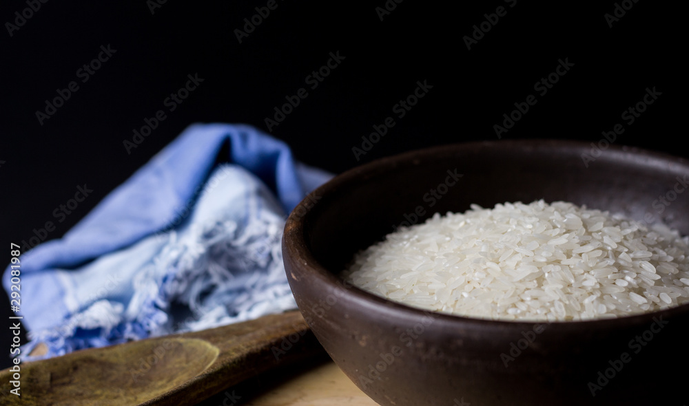 Uncooked rice in clay bowl on a wooden table with black background.