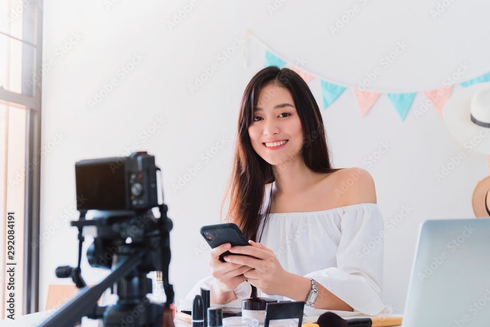 Asian beautiful women blogger are using the smartphone live streaming online with cosmatic in the white room with cosmetics on table.Concept of online shopping business. Asian beautiful women blogger are using the smartphone live streaming online with cosmatic in the white room with cosmetics on table.Concept of online shopping business.