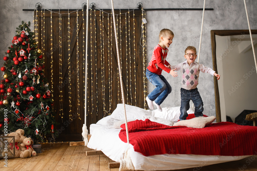 boys, brothers, have fun. jumping on  hanging bed, in room with Christmas tree cluttered with red balls