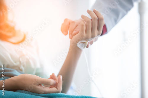 Hospitalized woman lying in bed while doctor checking examining his pulse. Doctor is checking patience's pulse by fingers, medical checking on bed. selective focus. have orange yellow flare.