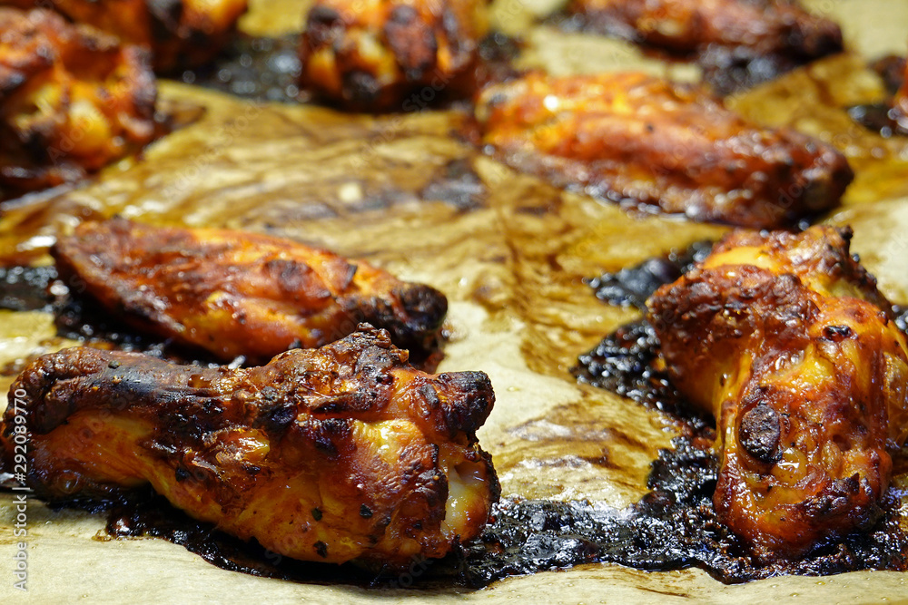 Close up of roasted spicy chicken wings on baking tray and cooking paper. Selective focus.