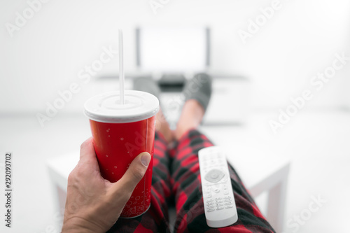 Man drinking soda juice and looking at TV with legs on the table in living room. photo