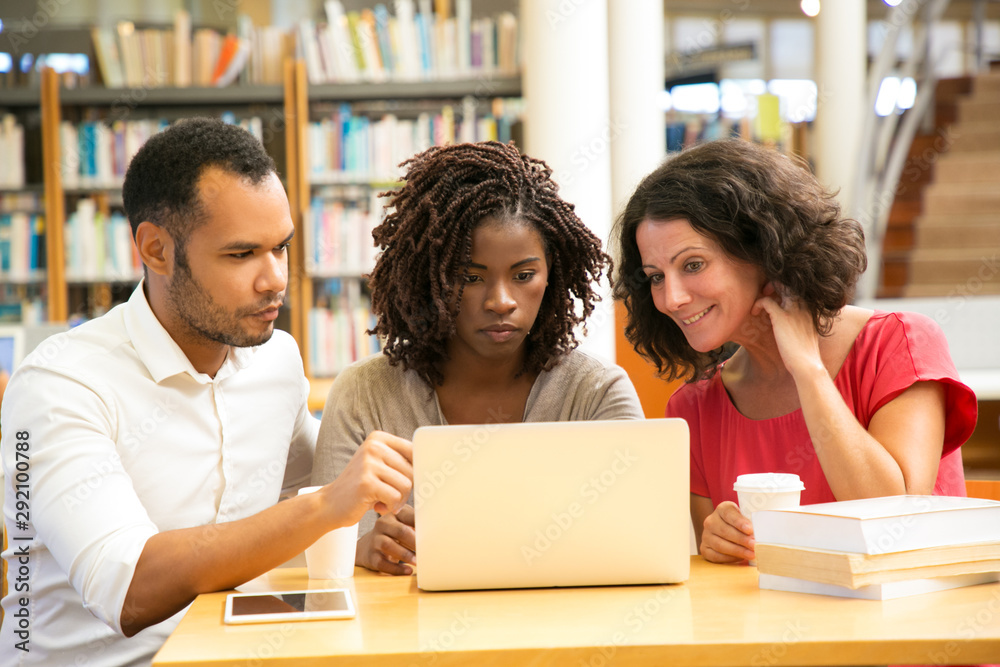 Front view of tired mature students looking at laptop. Thoughtful man and women sitting at table with modern devices. Education concept Front view of tired mature students looking at laptop. Thoughtful man and women sitting at table with modern devices. Education concept