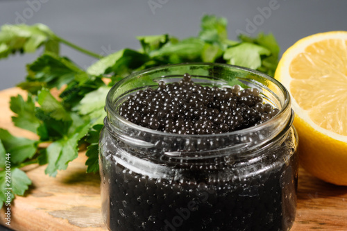 black and red caviar in glass jars with parsley and lemon on a gray background. Russian national cuisine